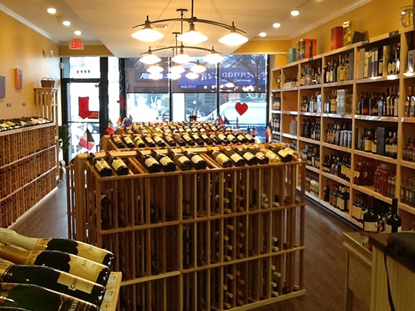 The image depicts a wine shop with numerous bottles of wine on display for sale, arranged on shelves behind the counter.