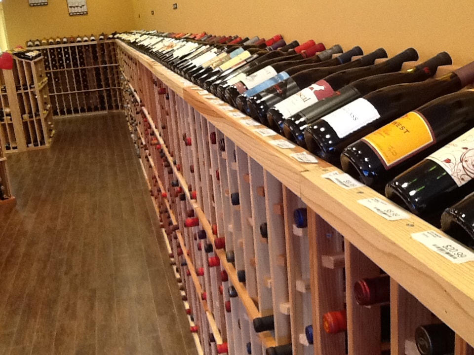 The image displays a well-stocked wine rack with numerous bottles of wine organized by type and vintage, showcasing an extensive selection for customers.